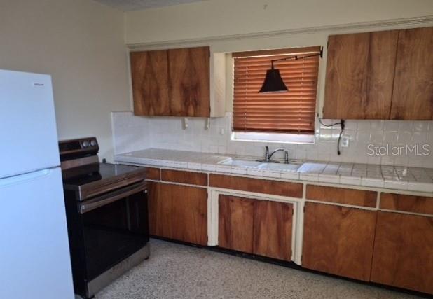A kitchen features wood cabinets, a white tiled countertop, a stainless steel stove, and a refrigerator — 639 N 75TH AVENUE N, ST PETERSBURG, FL