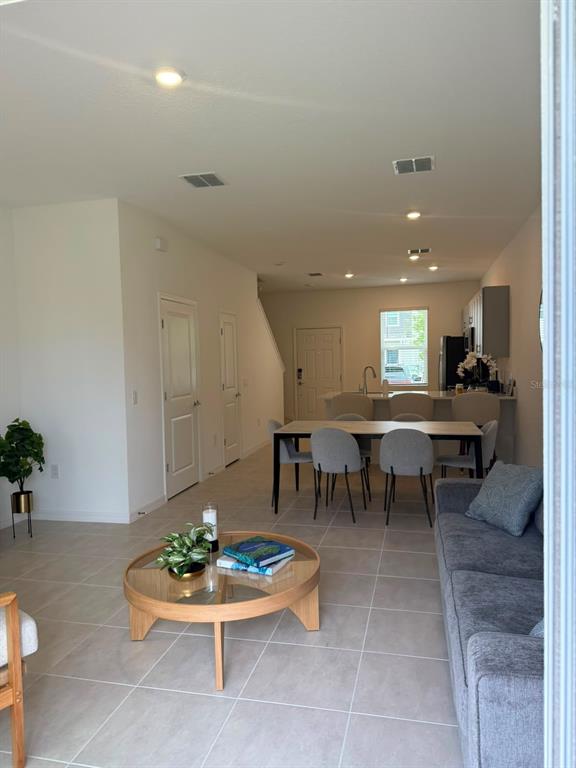 An open-concept living and dining area features light tile flooring and a neutral color palette — 3119 SKYLINE LOOP, POINCIANA, FL