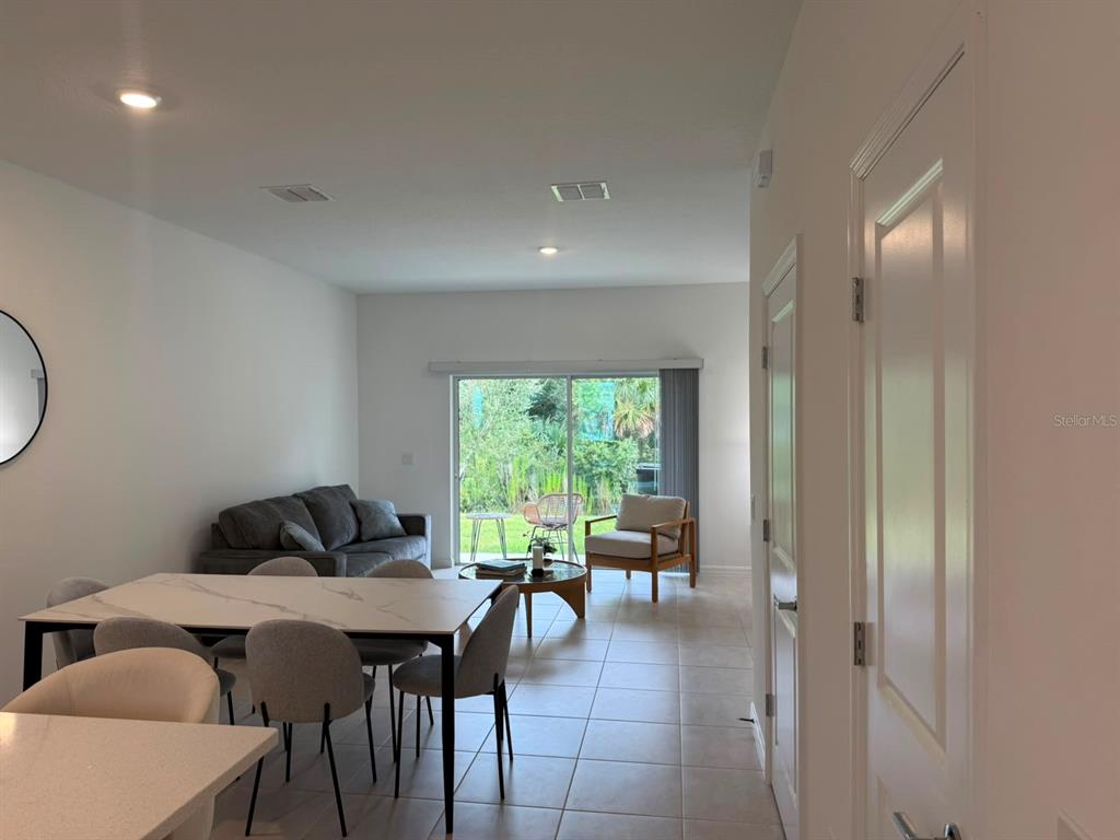 An open-concept living and dining area features tile flooring, a sliding glass door, and furniture — 3119 SKYLINE LOOP, POINCIANA, FL