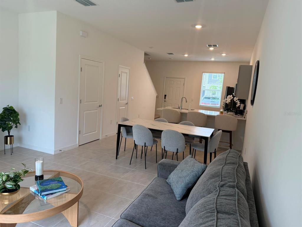 An open-concept living and dining area features tile flooring, a grey sofa, and kitchen island — 3119 SKYLINE LOOP, POINCIANA, FL