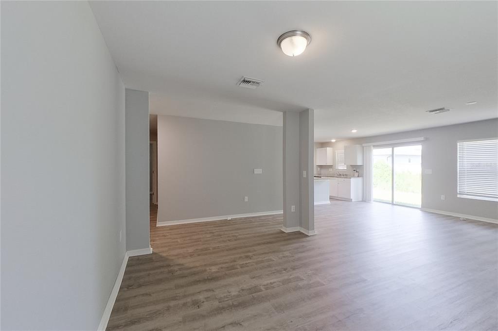 An open-concept living area features light gray walls, wood-look flooring, and a kitchen in back — 947 GRANT BOULEVARD, LEHIGH ACRES, FL