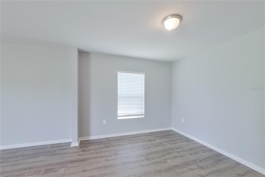 An empty room with light gray walls, wood-look flooring, a single window, and a ceiling light — 947 GRANT BOULEVARD, LEHIGH ACRES, FL
