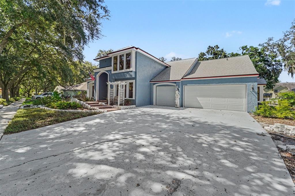 A blue two-story house with a three-car garage and a concrete driveway under large trees — 6203 FARTHING STREET, TAMPA, FL