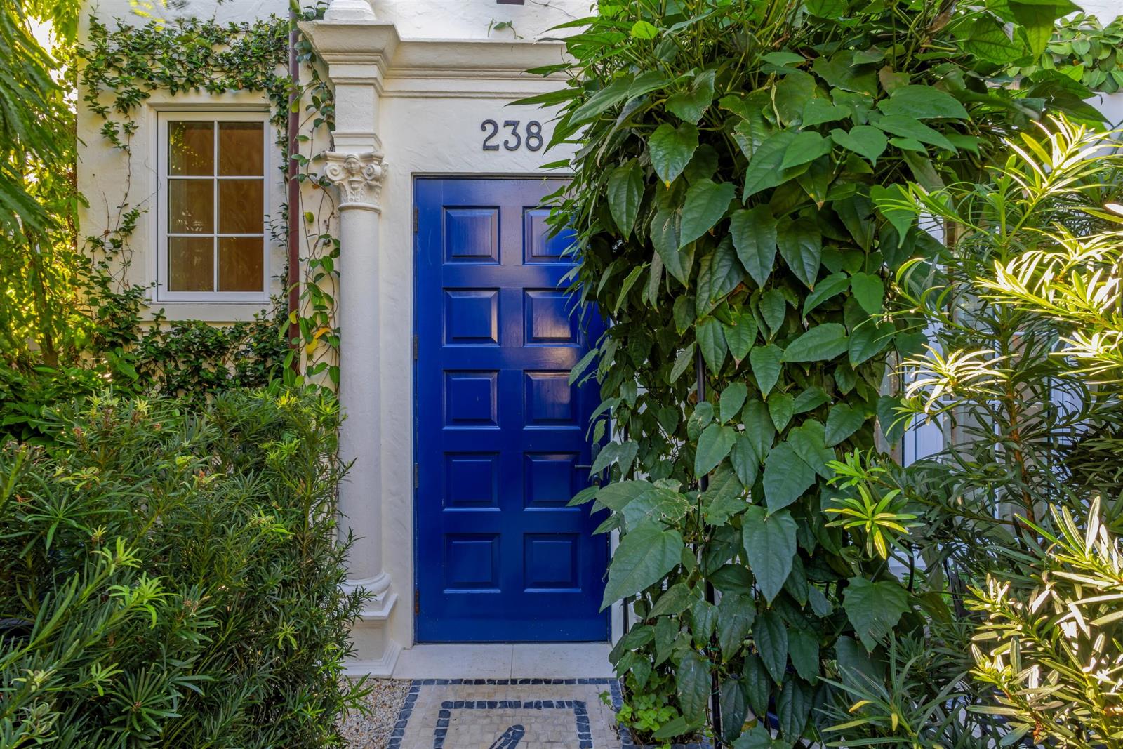 A bright blue paneled door is framed by white columns and lush green foliage — 238 Phipps Plaza, Palm Beach FL 33480, PALM BEACH, FL