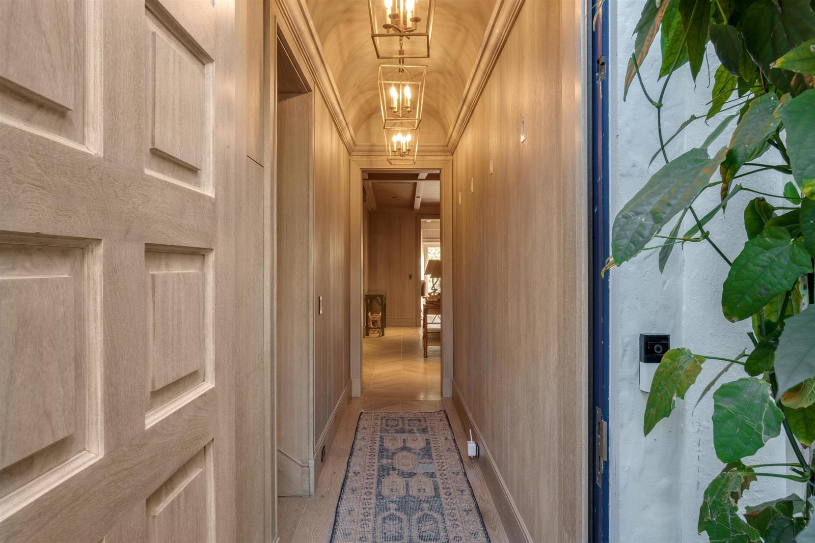 A hallway with wood-paneled walls, a vaulted ceiling, pendant lights, and a patterned runner rug — 238 Phipps Plaza, Palm Beach FL 33480, PALM BEACH, FL