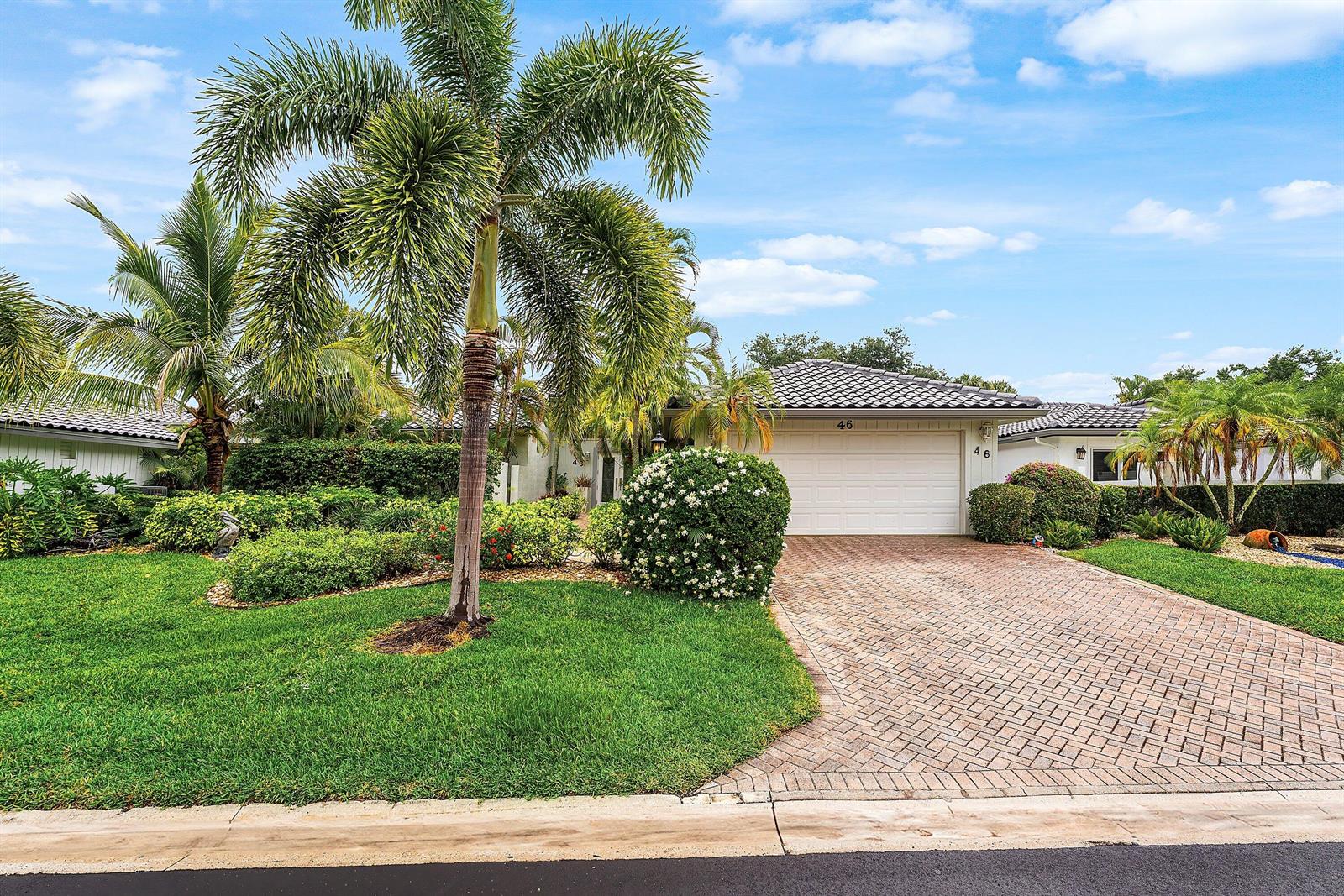 A single-story house with a white garage, brick driveway, and palm trees in the front yard — 46 Woods Lane, Boynton Beach FL 33436, BOYNTON BEACH, FL