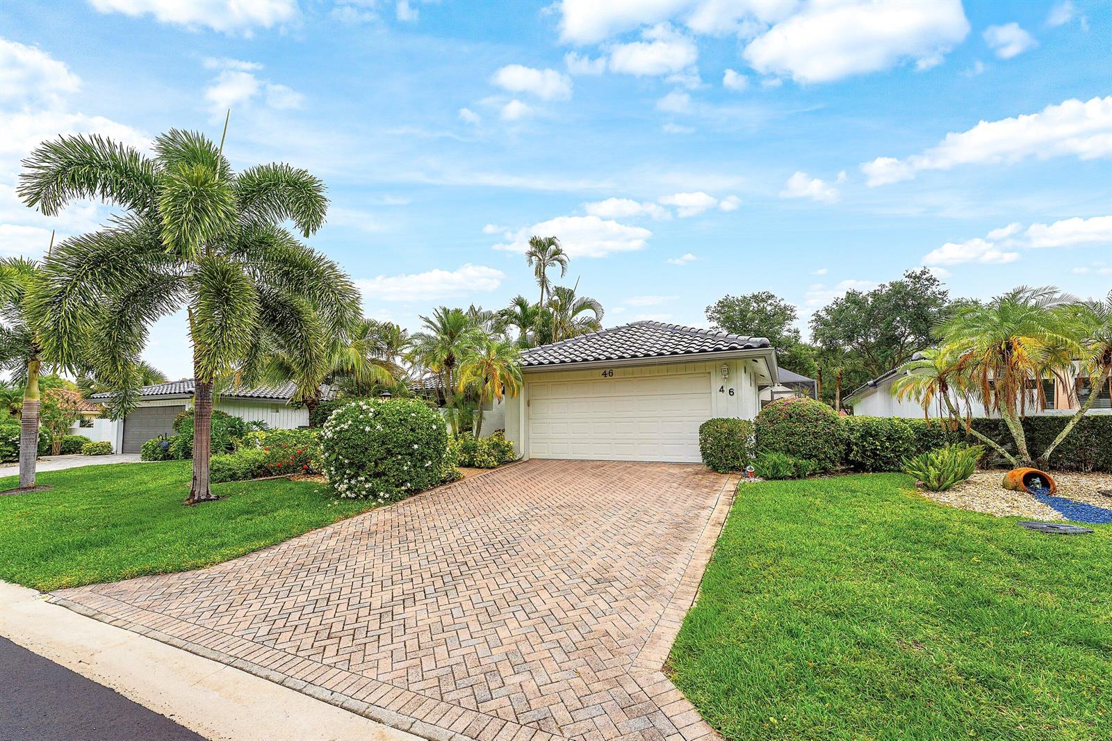 A single-story house with a white garage door and a paved driveway surrounded by landscaping — 46 Woods Lane, Boynton Beach FL 33436, BOYNTON BEACH, FL
