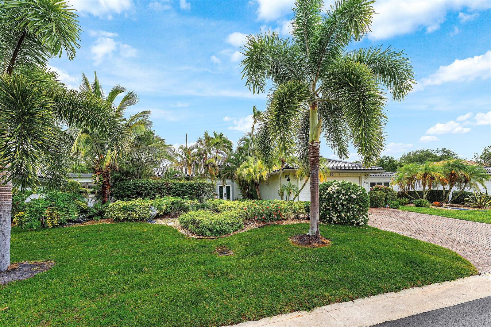 A single-story house with a paved driveway, lush landscaping, and several tall palm trees — 46 Woods Lane, Boynton Beach FL 33436, BOYNTON BEACH, FL