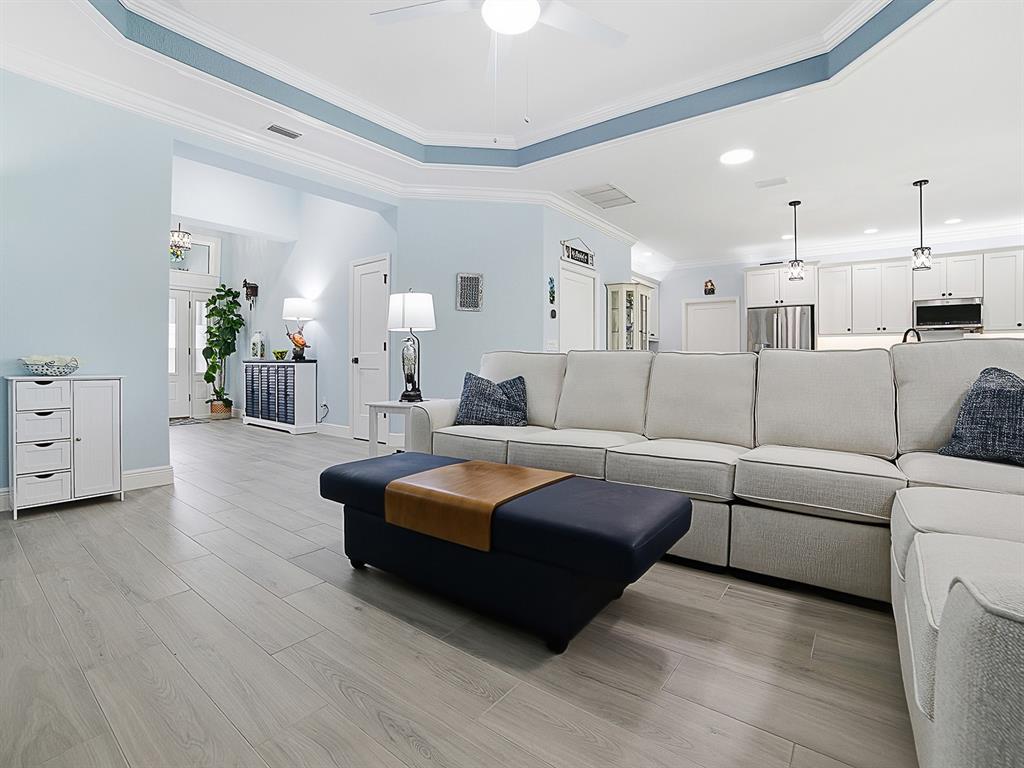 A living room features light blue walls, a tray ceiling, and a beige sectional sofa — 7004 EMILINE TERRACE, THE VILLAGES, FL