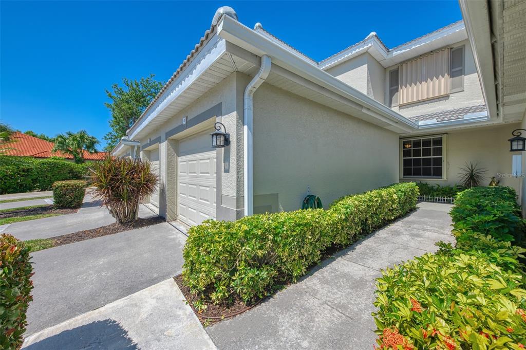 A view of a beige house exterior featuring a garage, a walkway, and manicured hedges — 3433 GRAND VISTA COURT UNIT 102, PORT CHARLOTTE, FL