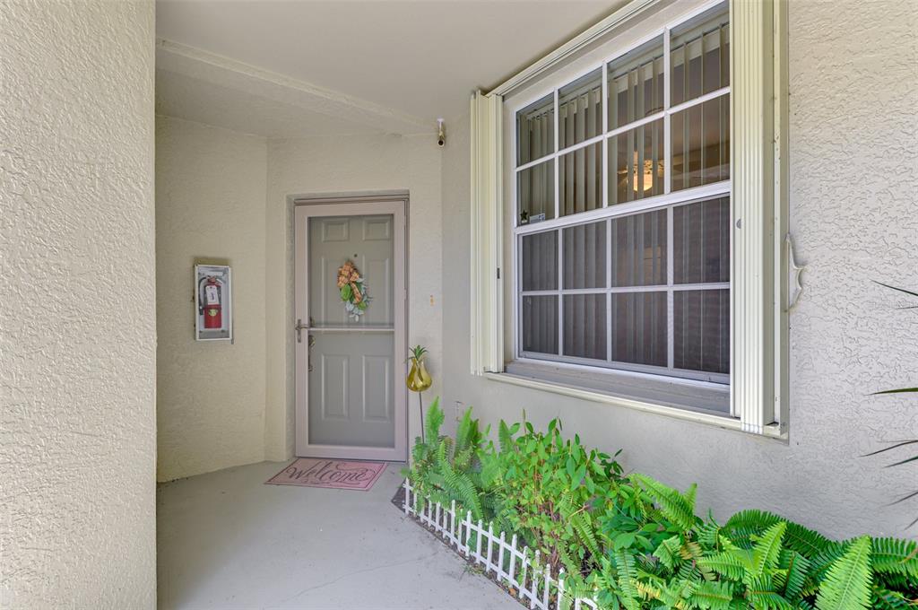 A covered entryway features a light-colored door with a wreath, a window, and potted ferns — 3433 GRAND VISTA COURT UNIT 102, PORT CHARLOTTE, FL
