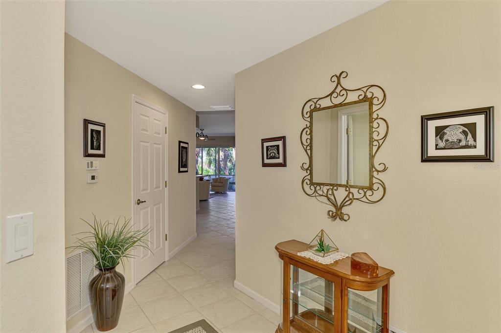 A hallway features tile flooring, a decorative mirror, a wooden console table, and wall art — 3433 GRAND VISTA COURT UNIT 102, PORT CHARLOTTE, FL