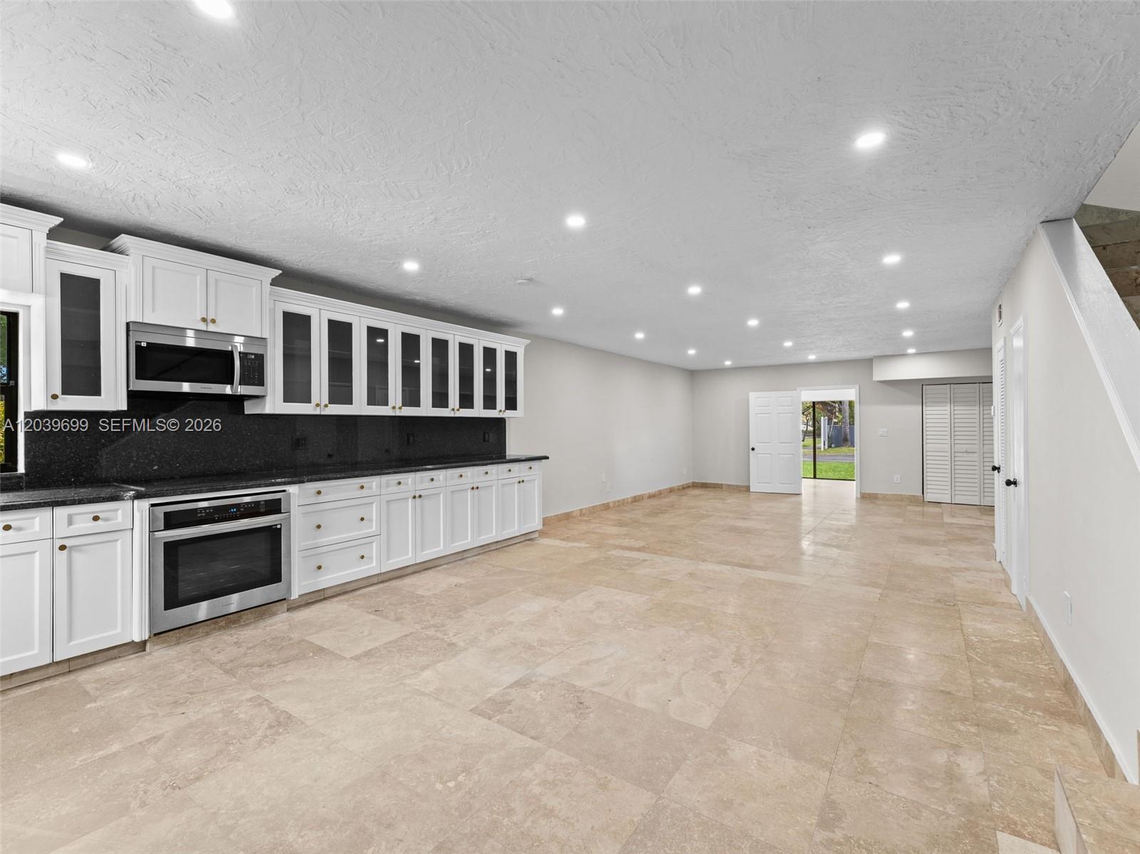 A kitchen with white cabinets, black countertops, and tile flooring opens into a spacious room — 13502 NE 24th Ct, North Miami FL 33181, NORTH MIAMI, FL