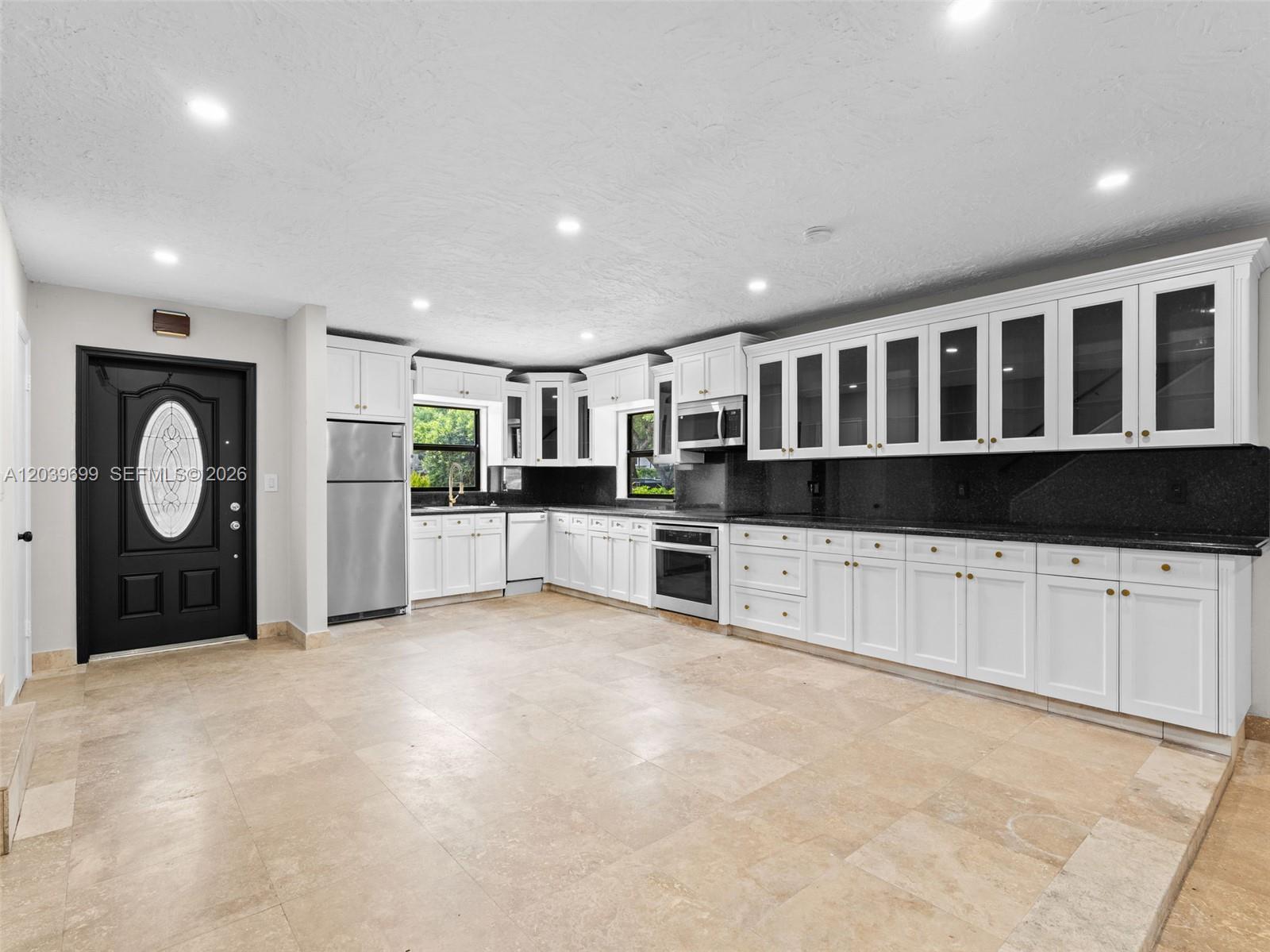 A kitchen features white cabinetry, black countertops, stainless steel appliances, and light-colored tile flooring — 13502 NE 24th Ct, North Miami FL 33181, NORTH MIAMI, FL
