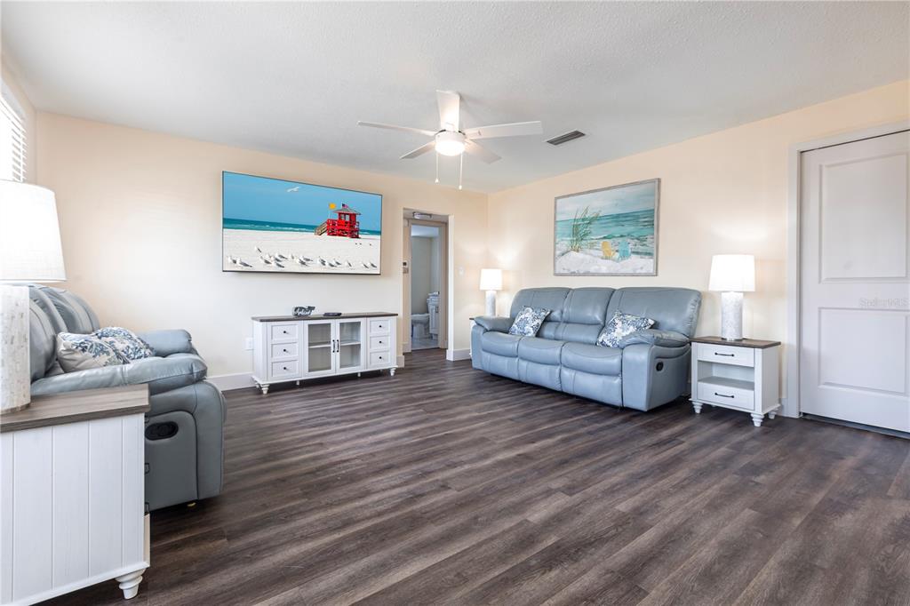 A living room features light blue leather sofas, wood-look flooring, and a beach-themed television display — 6020 MIDNIGHT PASS ROAD UNIT 52B, SARASOTA, FL