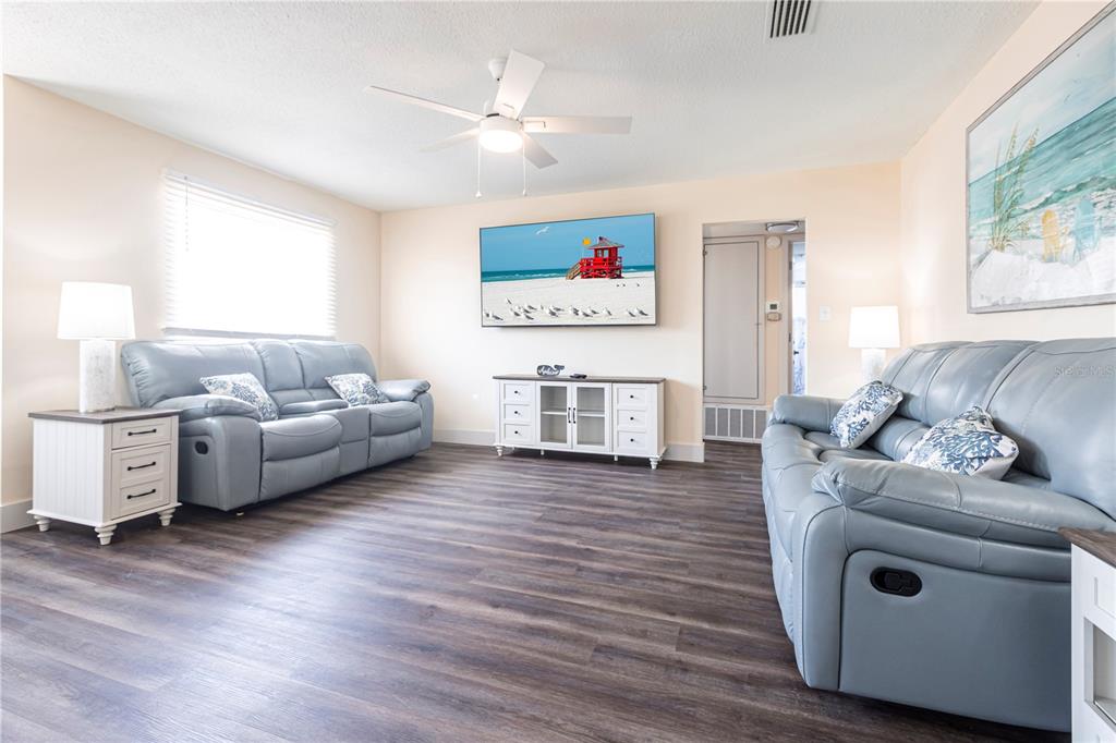 A living room features light blue leather sofas, wood-look flooring, and a wall-mounted television — 6020 MIDNIGHT PASS ROAD UNIT 52B, SARASOTA, FL