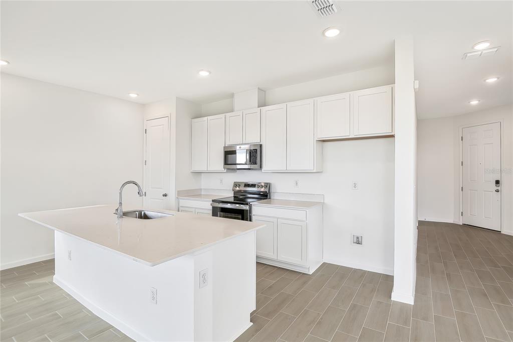 A kitchen features white cabinets, stainless steel appliances, a center island, and light-colored flooring — 1280 DAISY HILL AVENUE, DUNDEE, FL