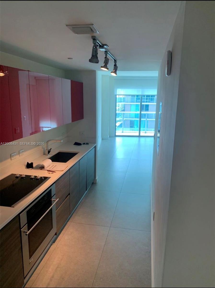A modern kitchen features dark wood-grain cabinetry, bright pink upper cabinets, and stainless steel appliances — 1100 S Miami Ave # 3705, Miami FL 33130, MIAMI, FL
