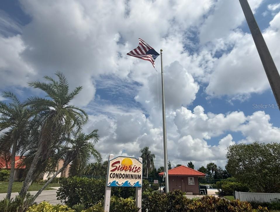 A sign for Sunrise Condominium stands next to a flagpole with an American flag — 6564 DRAW LANE UNIT 102, SARASOTA, FL
