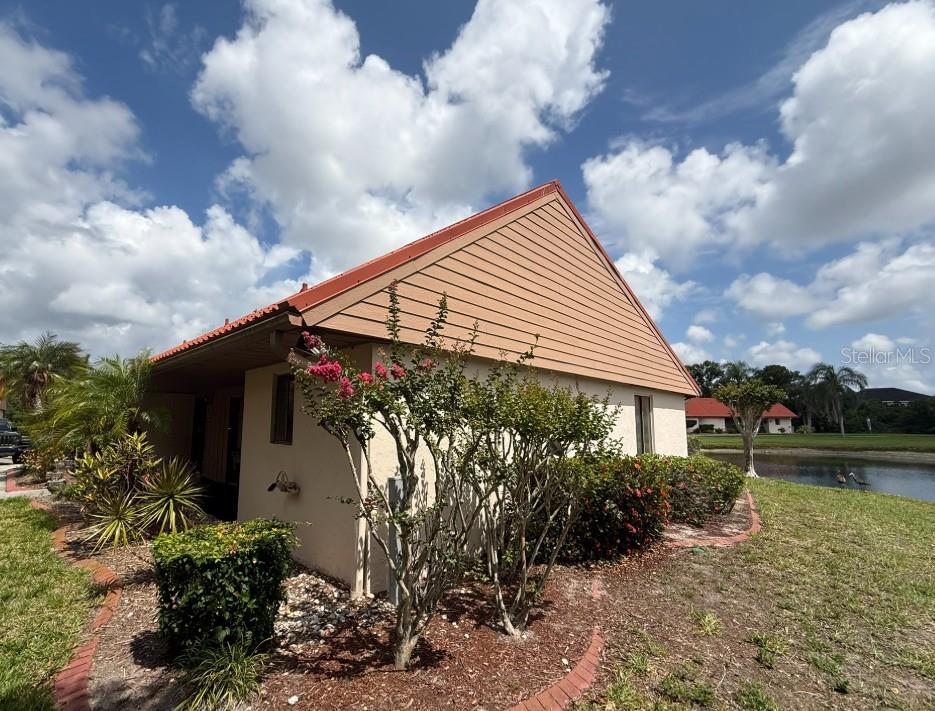 A side view of a tan house with a red roof and landscaping near a pond — 6564 DRAW LANE UNIT 102, SARASOTA, FL