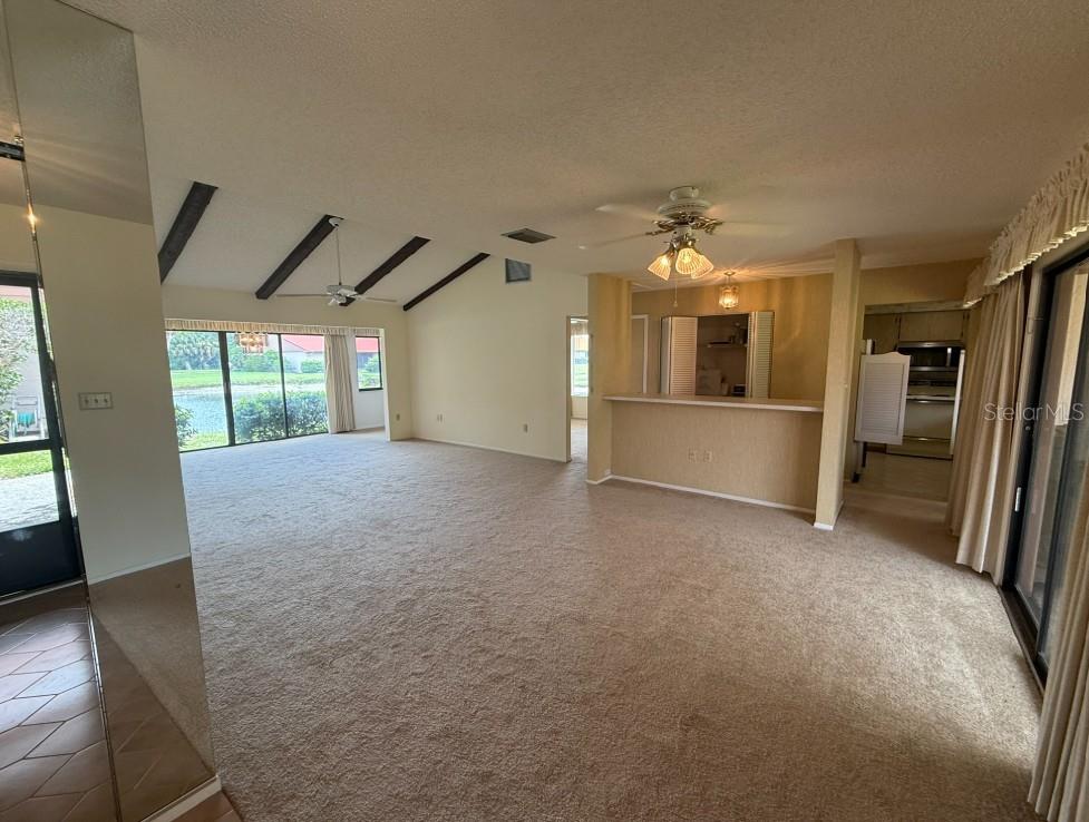 A carpeted living room features a vaulted ceiling with exposed beams and a breakfast bar — 6564 DRAW LANE UNIT 102, SARASOTA, FL