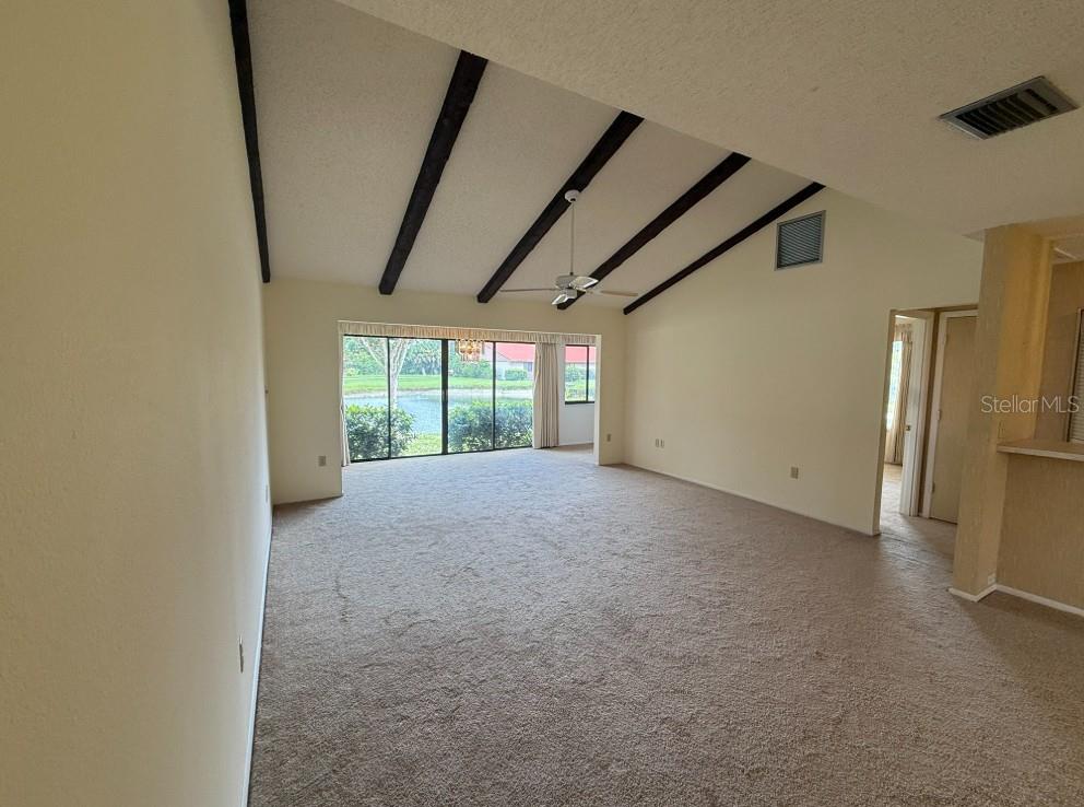 A living room with beige carpet, vaulted ceilings with exposed beams, and a sliding glass door — 6564 DRAW LANE UNIT 102, SARASOTA, FL