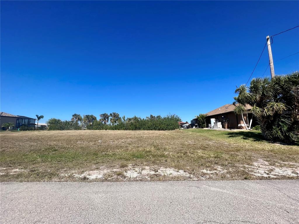 A vacant, grassy residential lot sits next to a house under a clear blue sky — 4221 NW 20TH TERRACE, CAPE CORAL, FL
