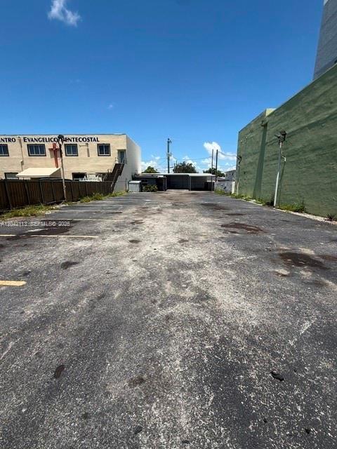 An empty paved parking lot sits between a tan building and a green wall — MIAMI, FL