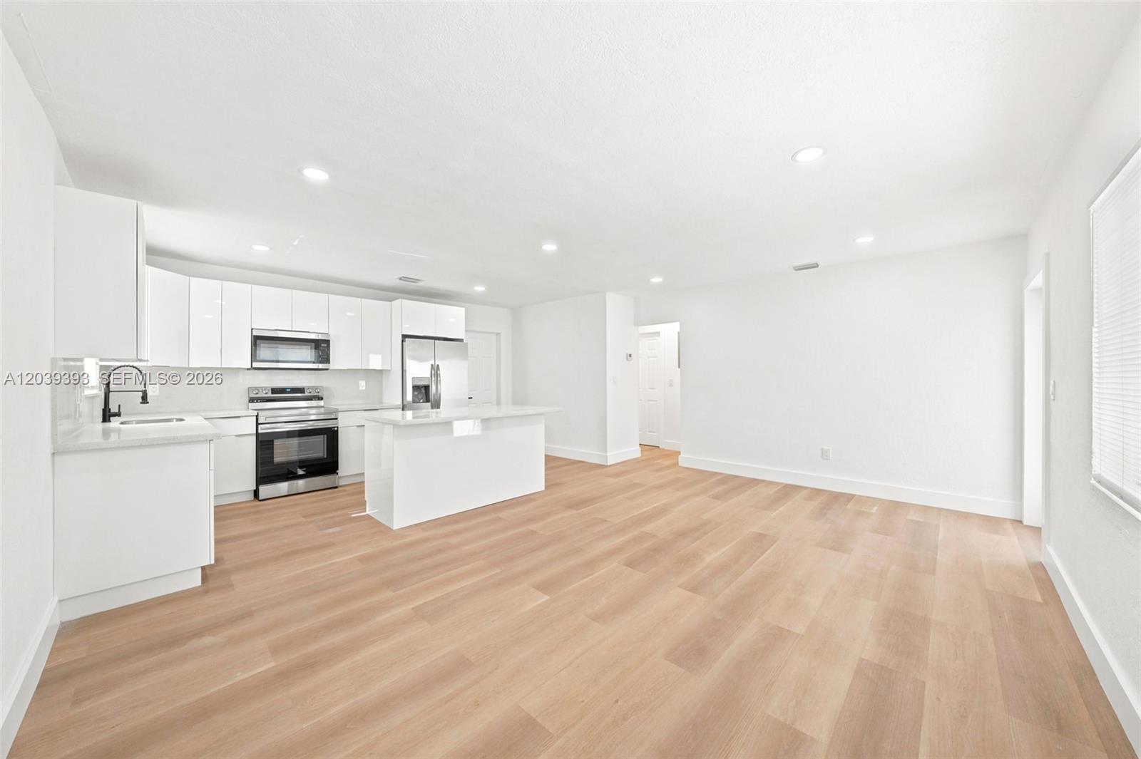 A modern, open-concept kitchen features white cabinetry, stainless steel appliances, and light wood flooring — 1491 NW 55th Ter, Miami FL 33142, MIAMI, FL