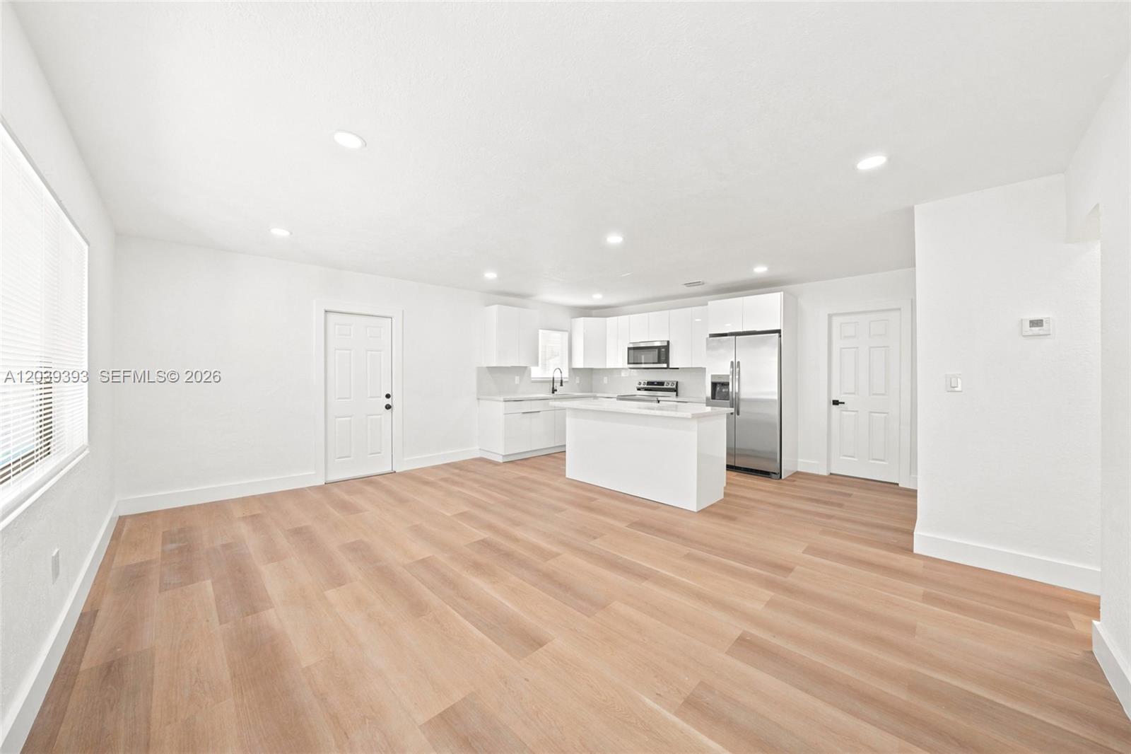This open-concept kitchen features white cabinetry, stainless steel appliances, and light wood-look flooring — 1491 NW 55th Ter, Miami FL 33142, MIAMI, FL