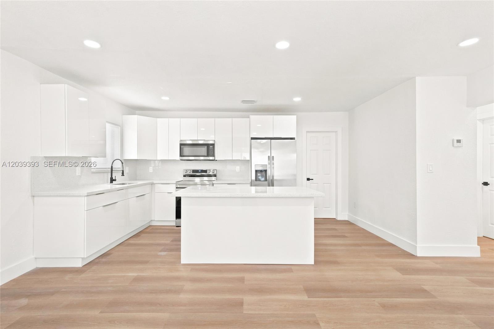 A modern kitchen features white cabinets, stainless steel appliances, and light wood-look flooring — 1491 NW 55th Ter, Miami FL 33142, MIAMI, FL