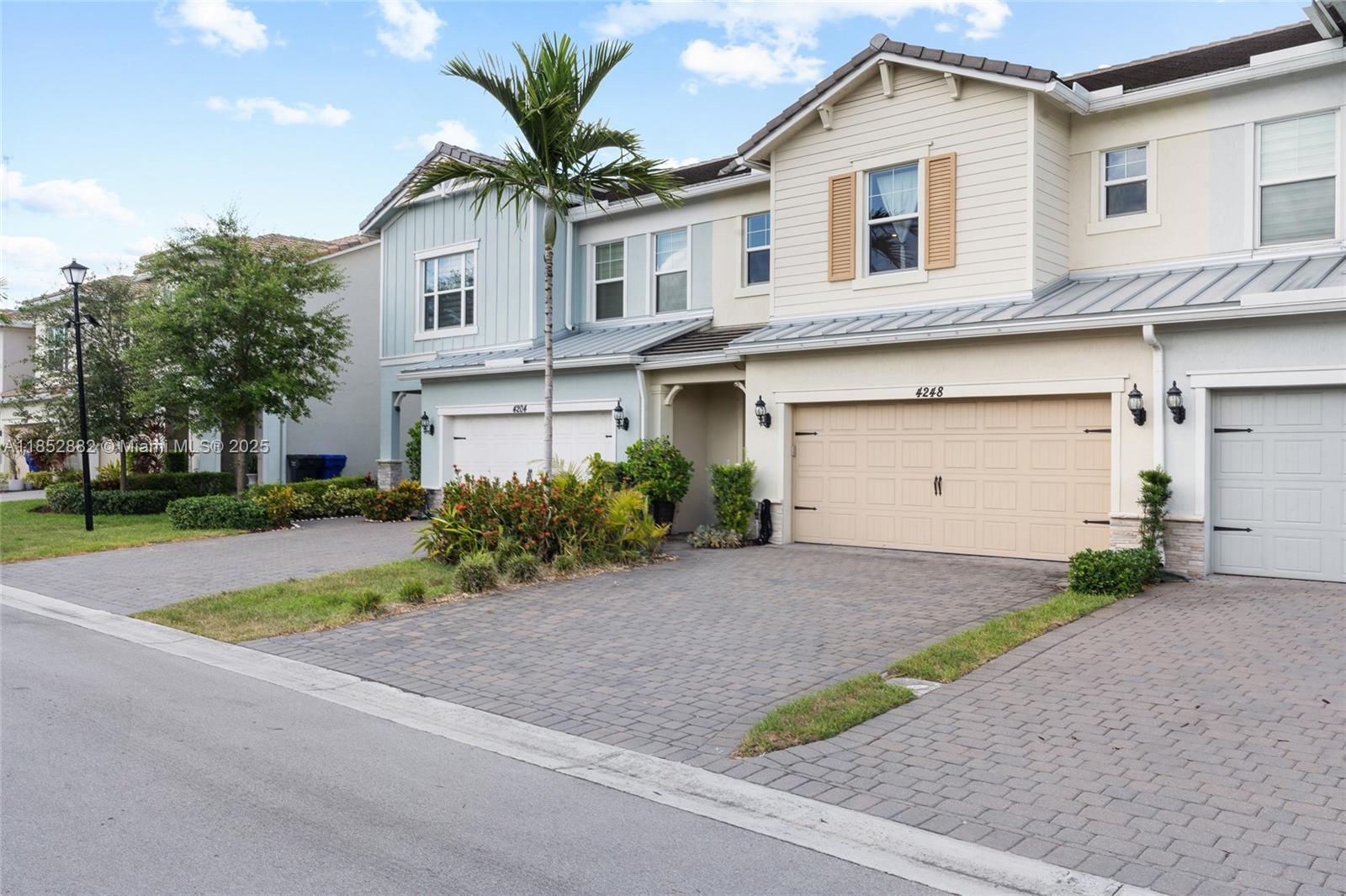 Two adjacent townhouses feature paved driveways, attached garages, and light-colored siding under a blue sky — 4248 Ficus St, Hollywood FL 33021, HOLLYWOOD, FL