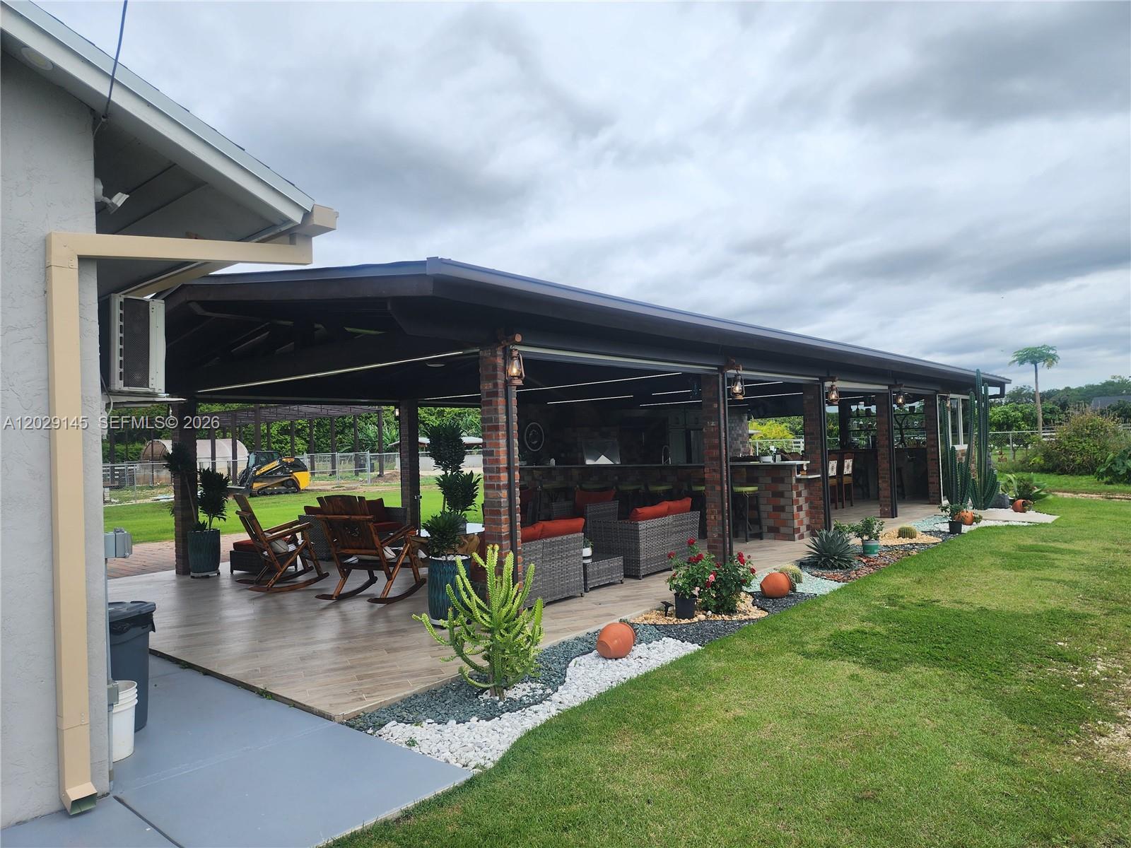 A covered outdoor patio features brick columns, wicker furniture, and a bar area with stools — HOMESTEAD, FL