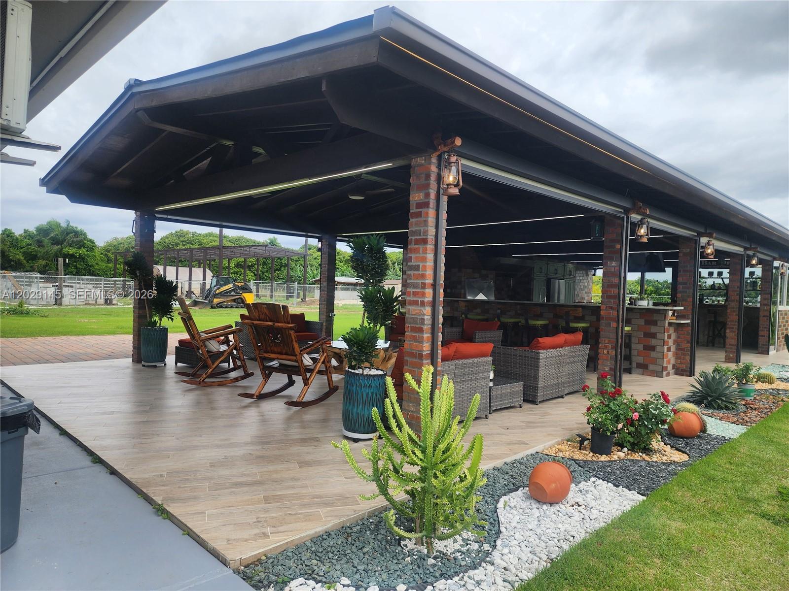 A covered outdoor patio features a brick-columned structure, lounge seating, and a built-in bar area — HOMESTEAD, FL
