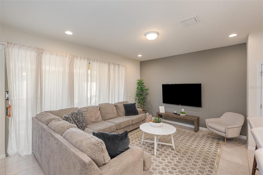 A living room features a large sectional sofa, a wall-mounted television, and a patterned area rug — 9025 RHODES STREET, KISSIMMEE, FL