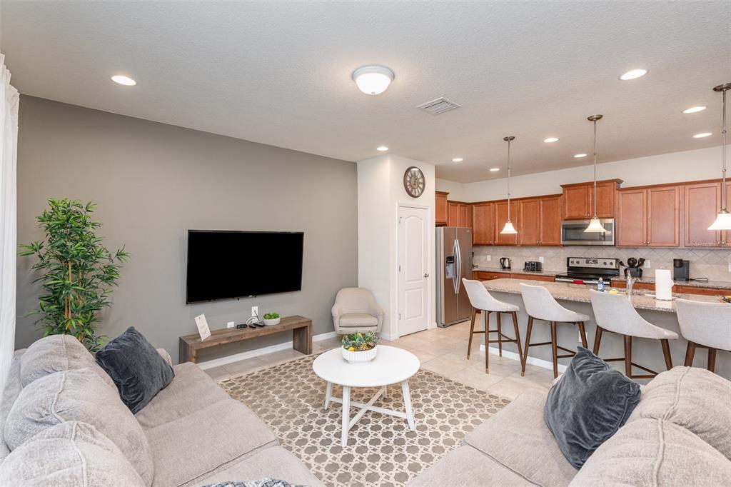A living room with a gray wall, mounted television, and an open kitchen with bar seating — 9025 RHODES STREET, KISSIMMEE, FL