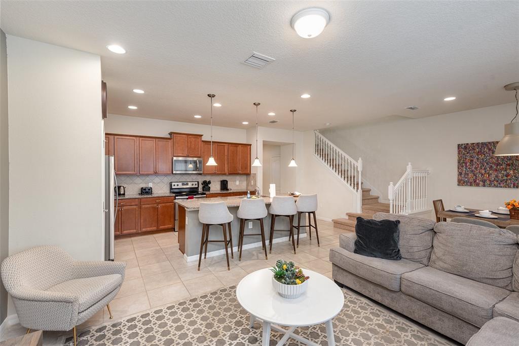 An open-concept kitchen and living area features wooden cabinets, a breakfast bar, and stairs — 9025 RHODES STREET, KISSIMMEE, FL