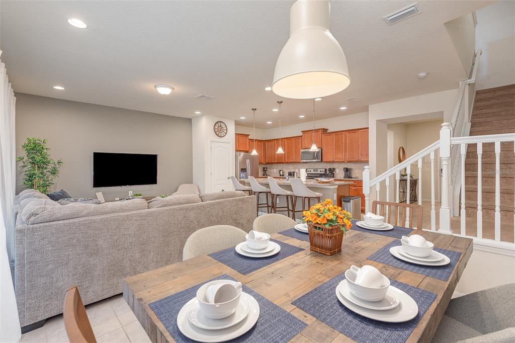 An open-concept living and dining area features a wooden table, kitchen island, and staircase — 9025 RHODES STREET, KISSIMMEE, FL
