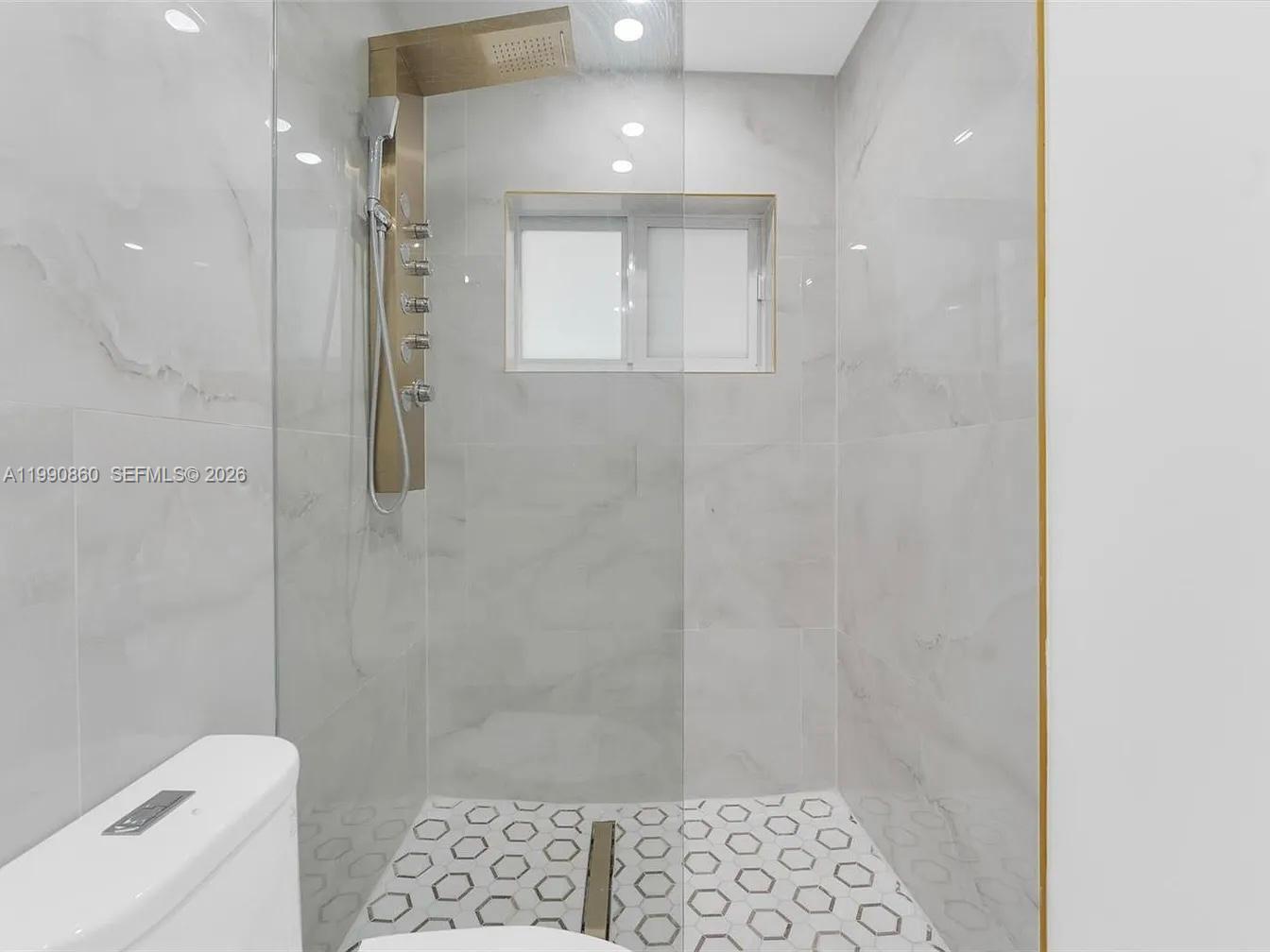 A walk-in shower features a gold rainfall shower panel, white marble-look tiles, and hexagonal flooring — 4900 NW 14th St, Lauderhill FL 33313, LAUDERHILL, FL