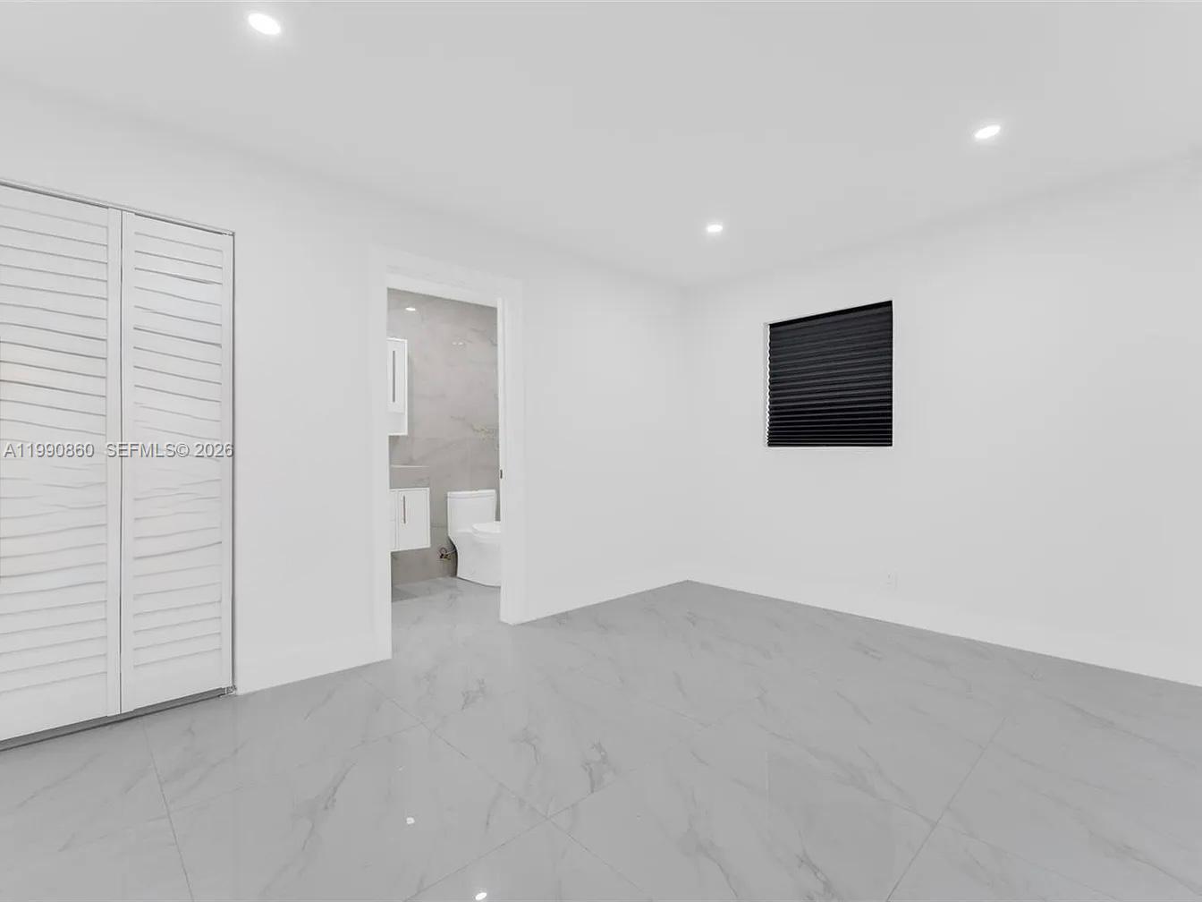 A minimalist bedroom features white walls, light gray tile flooring, and an attached bathroom — 4900 NW 14th St, Lauderhill FL 33313, LAUDERHILL, FL