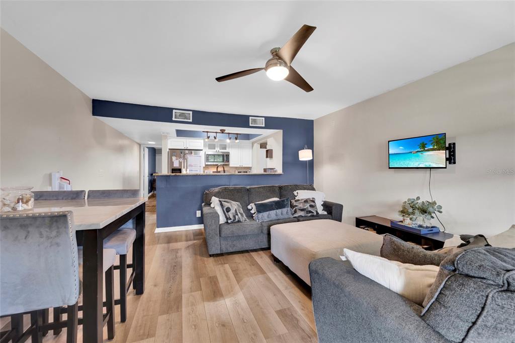 A living room with wood-look flooring, a gray sofa, and an open kitchen area — 2400 WINDING CREEK BOULEVARD UNIT 17-203, CLEARWATER, FL
