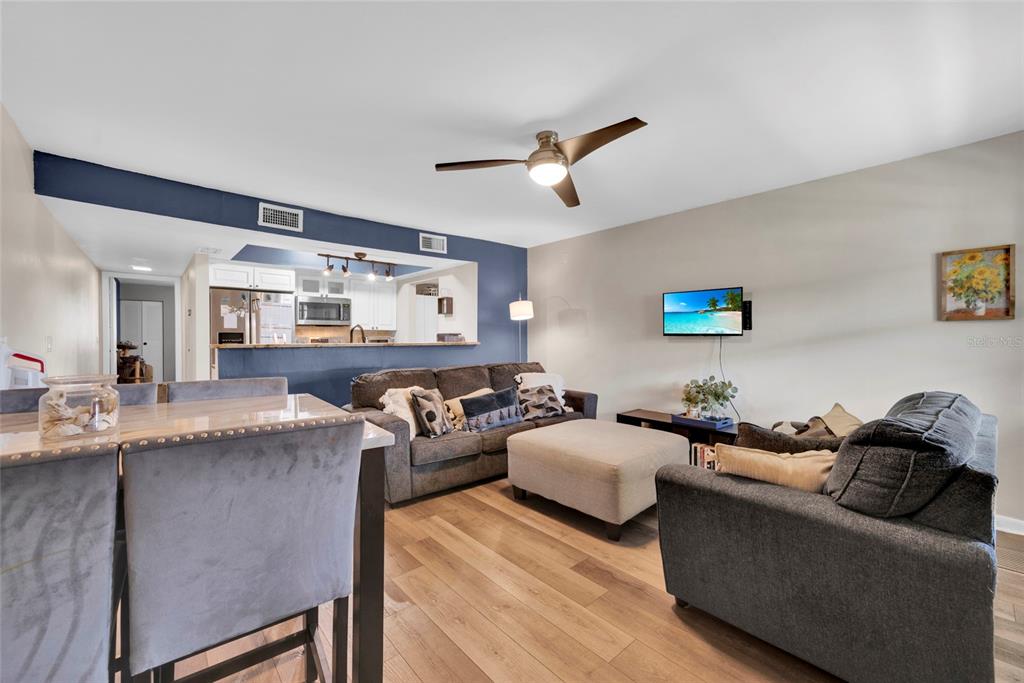 A living room with wood-look flooring, a gray sofa, and an open kitchen with blue walls — 2400 WINDING CREEK BOULEVARD UNIT 17-203, CLEARWATER, FL