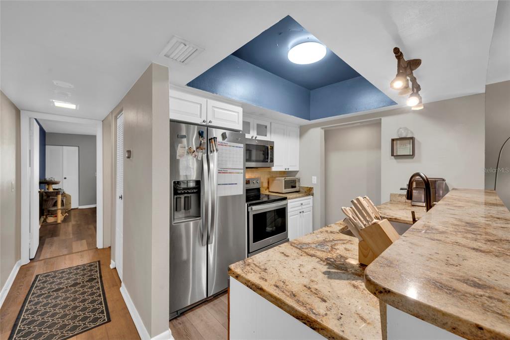 A kitchen features granite countertops, stainless steel appliances, and a blue tray ceiling with lighting — 2400 WINDING CREEK BOULEVARD UNIT 17-203, CLEARWATER, FL