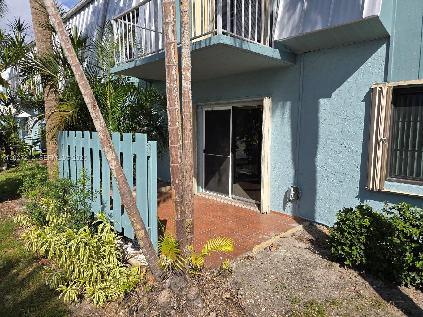 A ground-floor patio with a sliding glass door sits beside a blue wooden fence — 950 S Kanner Hwy # 4, Stuart FL 34994, STUART, FL