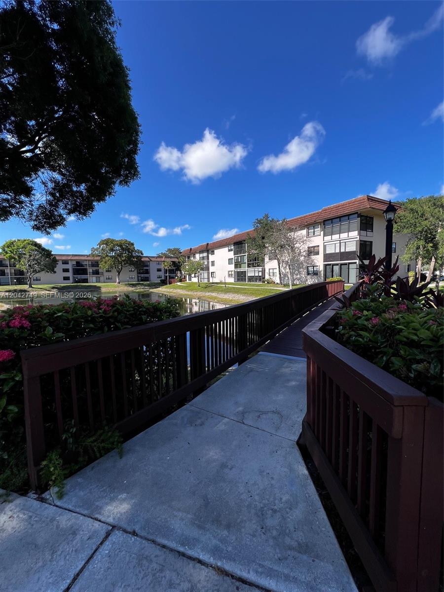 A wooden footbridge leads toward a multi-story apartment building overlooking a small pond — 4975 E Sabal Palm Blvd # 304, Tamarac FL 33319, TAMARAC, FL
