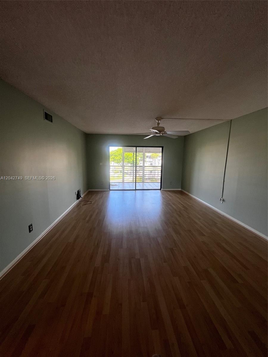 An empty room features light green walls, wood-look flooring, a ceiling fan, and sliding doors — 4975 E Sabal Palm Blvd # 304, Tamarac FL 33319, TAMARAC, FL