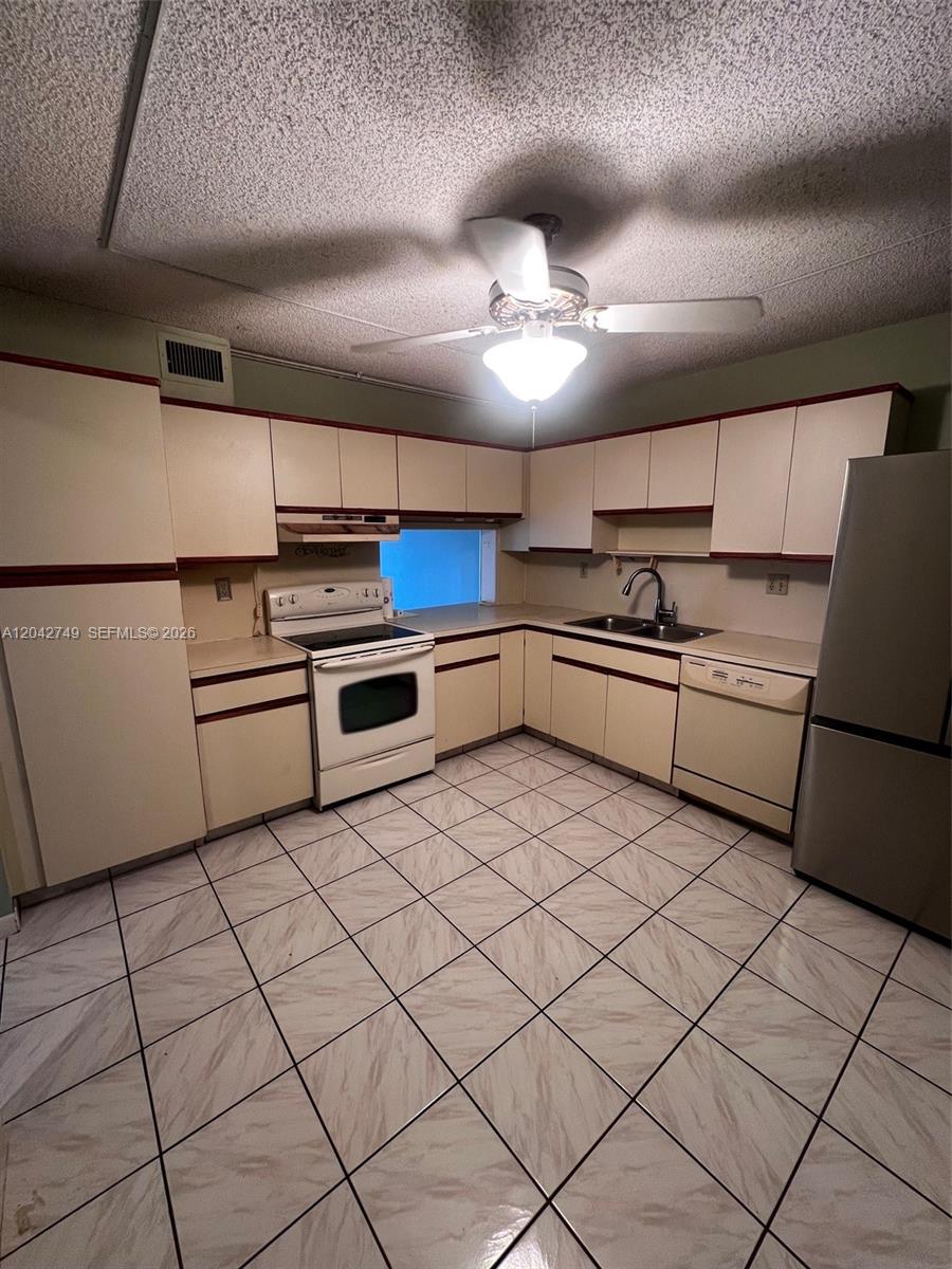 A kitchen features off-white cabinets with red trim, a ceiling fan, and tiled flooring — 4975 E Sabal Palm Blvd # 304, Tamarac FL 33319, TAMARAC, FL