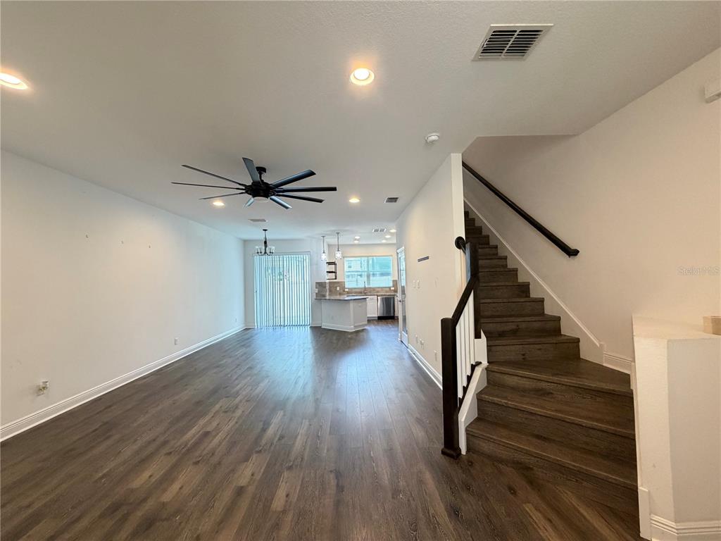 An open-concept living area features wood-look flooring, a ceiling fan, and a staircase — 2444 FOGGY CREEK CIRCLE, CLEARWATER, FL