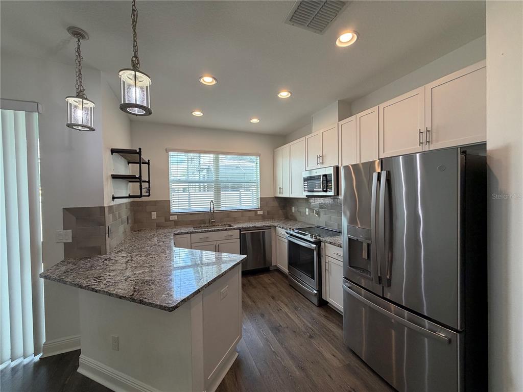 A modern kitchen features white cabinets, granite countertops, stainless steel appliances, and wood-look flooring — 2444 FOGGY CREEK CIRCLE, CLEARWATER, FL