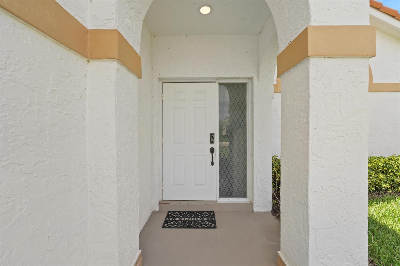 A white front door with a sidelight is framed by two stucco columns under an arch — 7015 SE Cutler Trail SE, Stuart FL 34997, STUART, FL